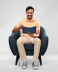 Image showing happy young indian man reading book in chair