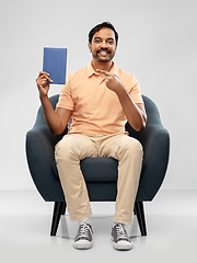 Image showing happy young indian man showing book in chair