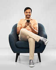 Image showing happy young indian man with smartphone in chair