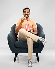 Image showing happy smiling indian man eating popcorn in chair