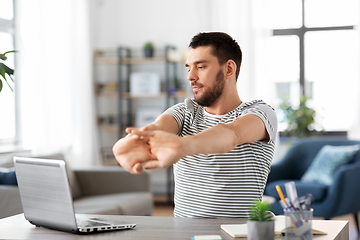 Image showing man with laptop stretching at home office