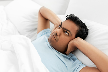 Image showing annoyed indian man lying in bed and closing ears