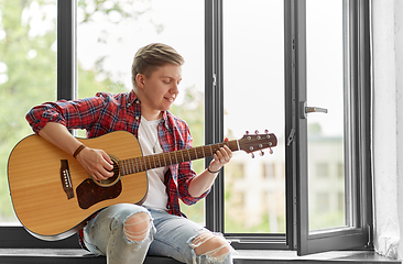 Image showing young man playing guitar sitting on windowsill