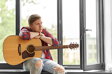 Image showing young man with guitar sitting on windowsill