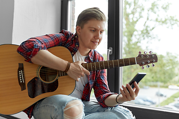 Image showing young man playing guitar sitting on windowsill