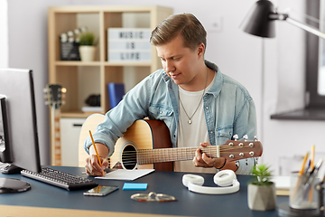 Image showing man with guitar writing to music book at home