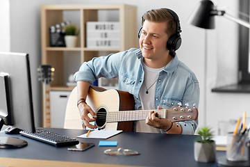 Image showing man in headphones playing guitar at home