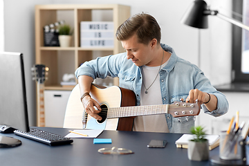 Image showing young man playing guitar sitting at table at home