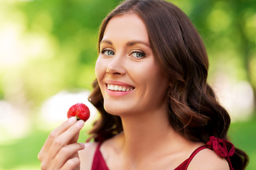 Image showing happy woman eating strawberry at summer park