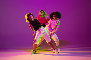 Image showing Sportive girls dancing hip-hop in stylish clothes on gradient background at dance hall in neon light