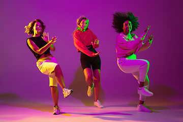 Image showing Sportive girls dancing hip-hop in stylish clothes on gradient background at dance hall in neon light