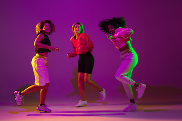 Image showing Sportive girls dancing hip-hop in stylish clothes on gradient background at dance hall in neon light