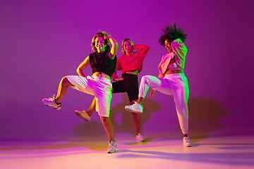 Image showing Sportive girls dancing hip-hop in stylish clothes on gradient background at dance hall in neon light