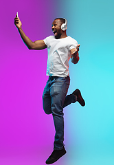 Image showing African-american young man\'s portrait on gradient studio background in neon, jumping high