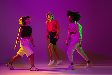 Image showing Sportive girls dancing hip-hop in stylish clothes on gradient background at dance hall in neon light