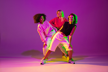 Image showing Sportive girls dancing hip-hop in stylish clothes on gradient background at dance hall in neon light