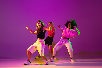 Image showing Sportive girls dancing hip-hop in stylish clothes on gradient background at dance hall in neon light