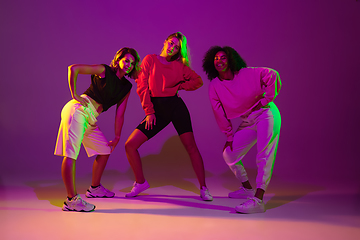 Image showing Sportive girls dancing hip-hop in stylish clothes on gradient background at dance hall in neon light