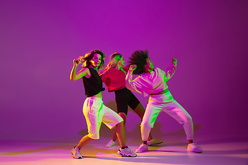 Image showing Sportive girls dancing hip-hop in stylish clothes on gradient background at dance hall in neon light