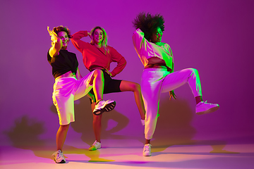 Image showing Sportive girls dancing hip-hop in stylish clothes on gradient background at dance hall in neon light