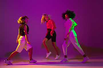 Image showing Sportive girls dancing hip-hop in stylish clothes on gradient background at dance hall in neon light