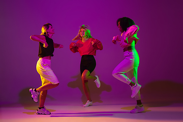 Image showing Sportive girls dancing hip-hop in stylish clothes on gradient background at dance hall in neon light