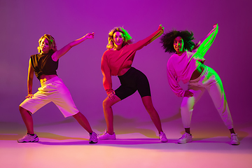 Image showing Sportive girls dancing hip-hop in stylish clothes on gradient background at dance hall in neon light