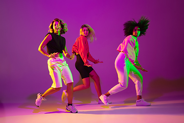 Image showing Sportive girls dancing hip-hop in stylish clothes on gradient background at dance hall in neon light