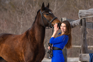 Image showing A beautiful girl with a horse is standing near an old wooden fence