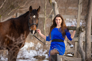 Image showing A beautiful girl is sitting on a log against the background of wooden ruins, a horse is standing nearby