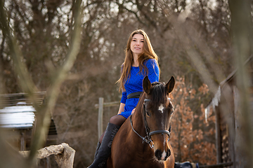 Image showing A girl in a blue dress sits on a horse against the backdrop of a winter forest