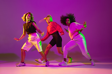 Image showing Sportive girls dancing hip-hop in stylish clothes on gradient background at dance hall in neon light