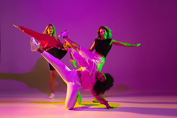 Image showing Sportive girls dancing hip-hop in stylish clothes on gradient background at dance hall in neon light