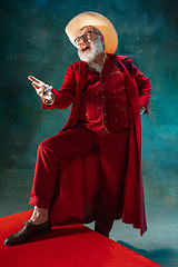 Image showing Modern stylish Santa Claus in red fashionable suit and cowboy\'s hat on dark background