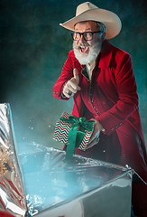 Image showing Modern stylish Santa Claus in red fashionable suit and cowboy\'s hat on dark background