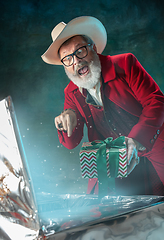 Image showing Modern stylish Santa Claus in red fashionable suit and cowboy\'s hat on dark background