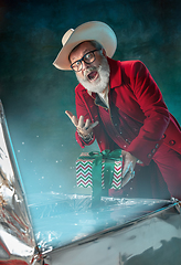 Image showing Modern stylish Santa Claus in red fashionable suit and cowboy\'s hat on dark background