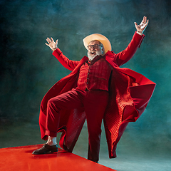 Image showing Modern stylish Santa Claus in red fashionable suit and cowboy\'s hat on dark background