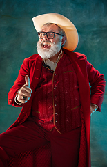 Image showing Modern stylish Santa Claus in red fashionable suit and cowboy\'s hat on dark background