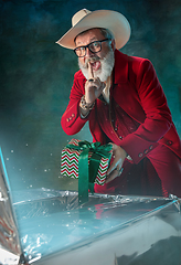 Image showing Modern stylish Santa Claus in red fashionable suit and cowboy\'s hat on dark background