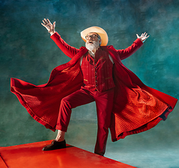 Image showing Modern stylish Santa Claus in red fashionable suit and cowboy\'s hat on dark background