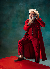 Image showing Modern stylish Santa Claus in red fashionable suit and cowboy\'s hat on dark background