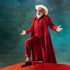 Image showing Modern stylish Santa Claus in red fashionable suit and cowboy\'s hat on dark background