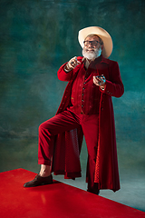 Image showing Modern stylish Santa Claus in red fashionable suit and cowboy\'s hat on dark background