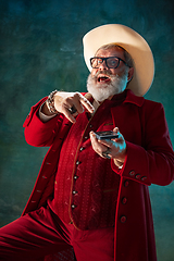 Image showing Modern stylish Santa Claus in red fashionable suit and cowboy\'s hat on dark background