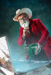 Image showing Modern stylish Santa Claus in red fashionable suit and cowboy\'s hat on dark background