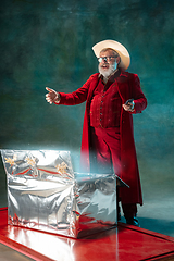 Image showing Modern stylish Santa Claus in red fashionable suit and cowboy\'s hat on dark background