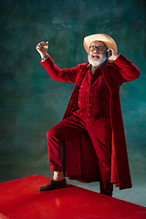 Image showing Modern stylish Santa Claus in red fashionable suit and cowboy\'s hat on dark background