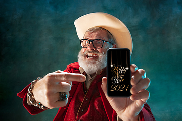 Image showing Modern stylish Santa Claus in red fashionable suit and cowboy\'s hat on dark background