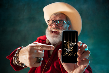 Image showing Modern stylish Santa Claus in red fashionable suit and cowboy\'s hat on dark background